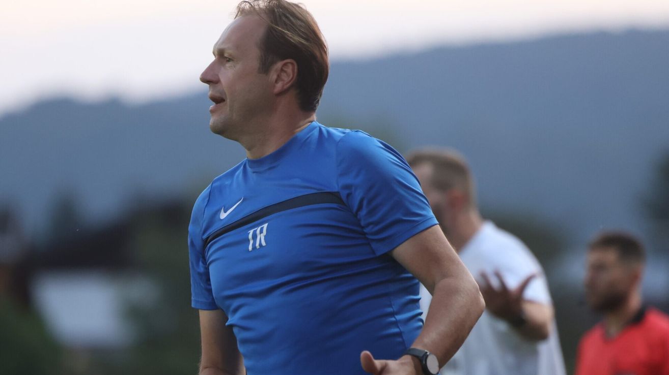 Ein Mann in einem blauen Nike-Shirt joggt im Freien, während ein anderer Mann in einem weißen Shirt hinter ihm steht.