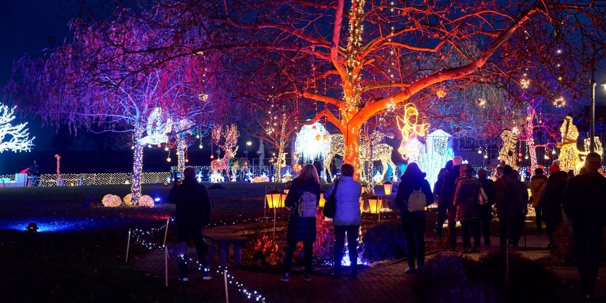 Menschen versammeln sich um einen geschmückten Baum mit Lichterketten und Ornamenten, einige machen Fotos und andere bewundern die Dekoration.