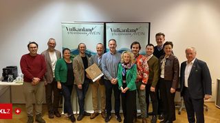 Eine Gruppe von Personen posiert für ein Foto vor einem Vulkanland Steiermark Wein-Banner. Die Frau in der Mitte hält einen Preis.