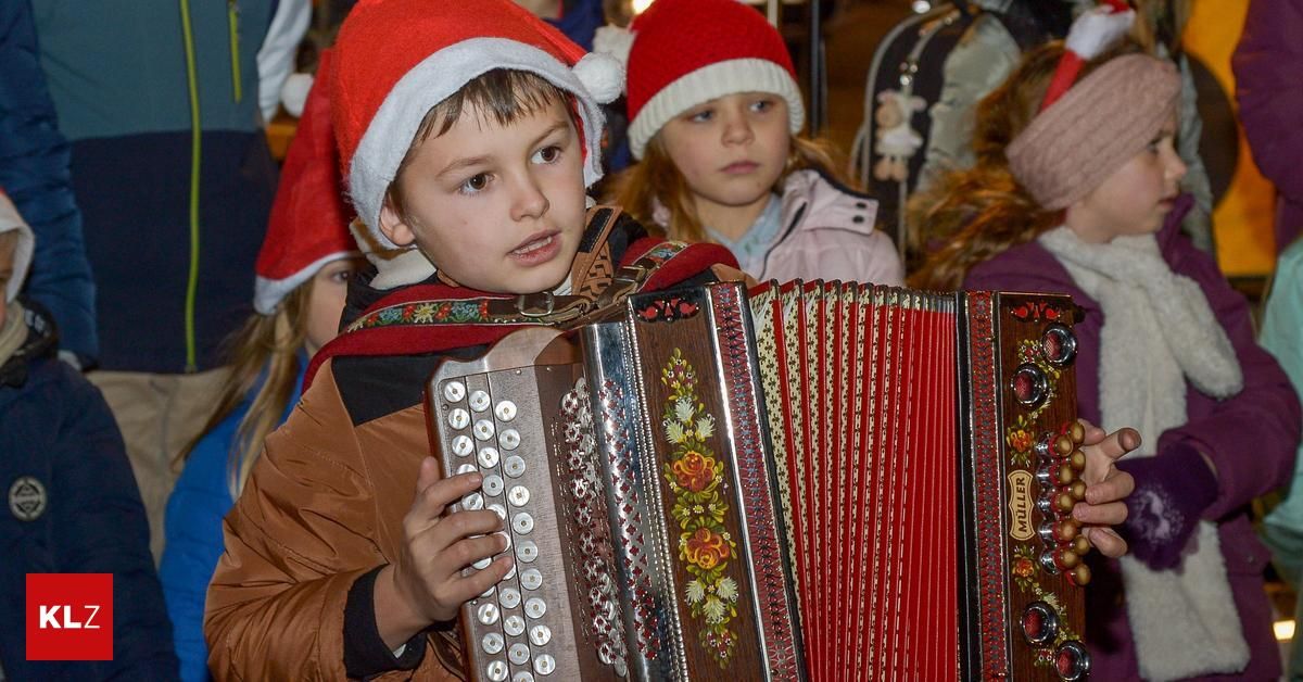 Ein junger Junge in einem Weihnachtsmannhut spielt ein Akkordeon vor einer Gruppe von Kindern.