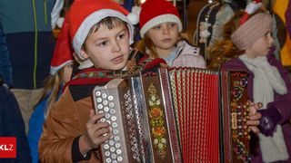 Ein junger Junge in einem Weihnachtsmannhut spielt ein Akkordeon vor einer Gruppe von Kindern.