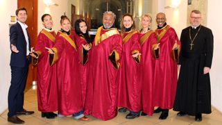 Ein Chor in roten und goldenen Roben, mit einem Mann und sechs Frauen, posiert für ein Foto.