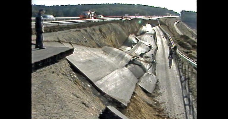 Eine Straße mit einem beschädigten Abschnitt, der erhebliche Erosion und Verschiebung der Straßenoberfläche zeigt.