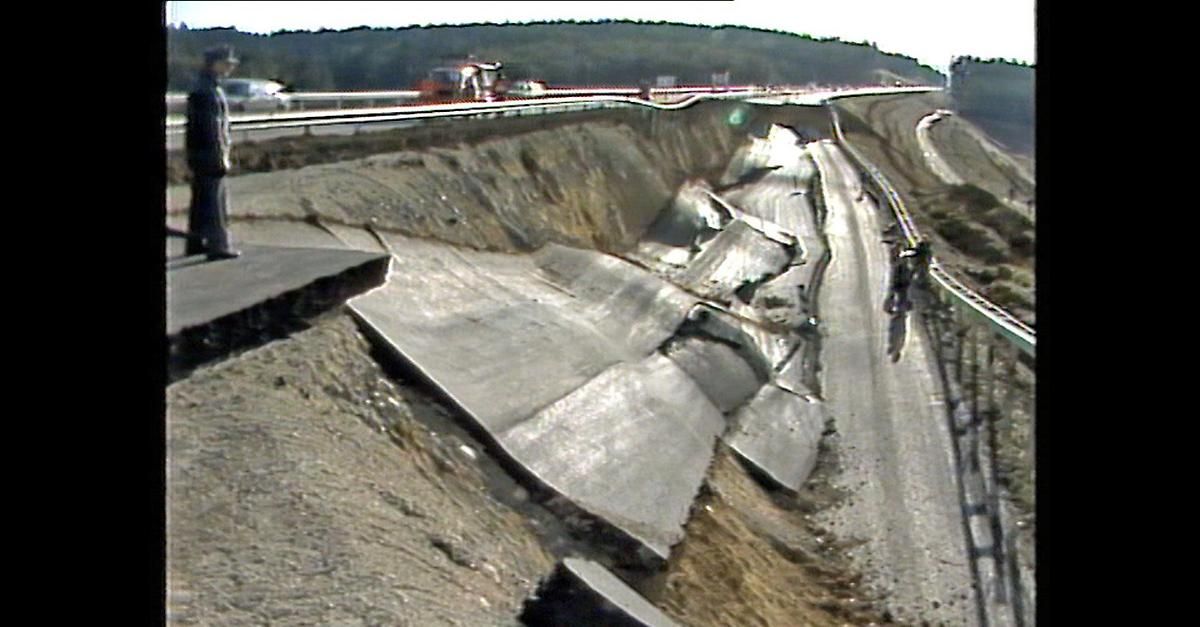 Eine Straße mit einem beschädigten Abschnitt, der erhebliche Erosion und Verschiebung der Straßenoberfläche zeigt.