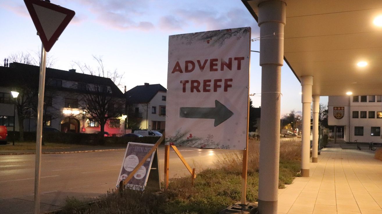 Ein weißes Schild mit roten Buchstaben steht auf einem Pfosten neben einem Bürgersteig und zeigt mit einem Pfeil nach rechts. Dahinter stehen Häuser und Bäume.