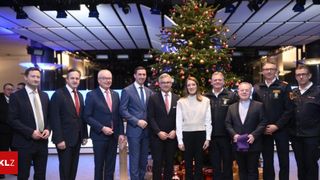 A group of formally dressed individuals, including men and a woman, are posing for a photograph in front of a decorated Christmas tree.