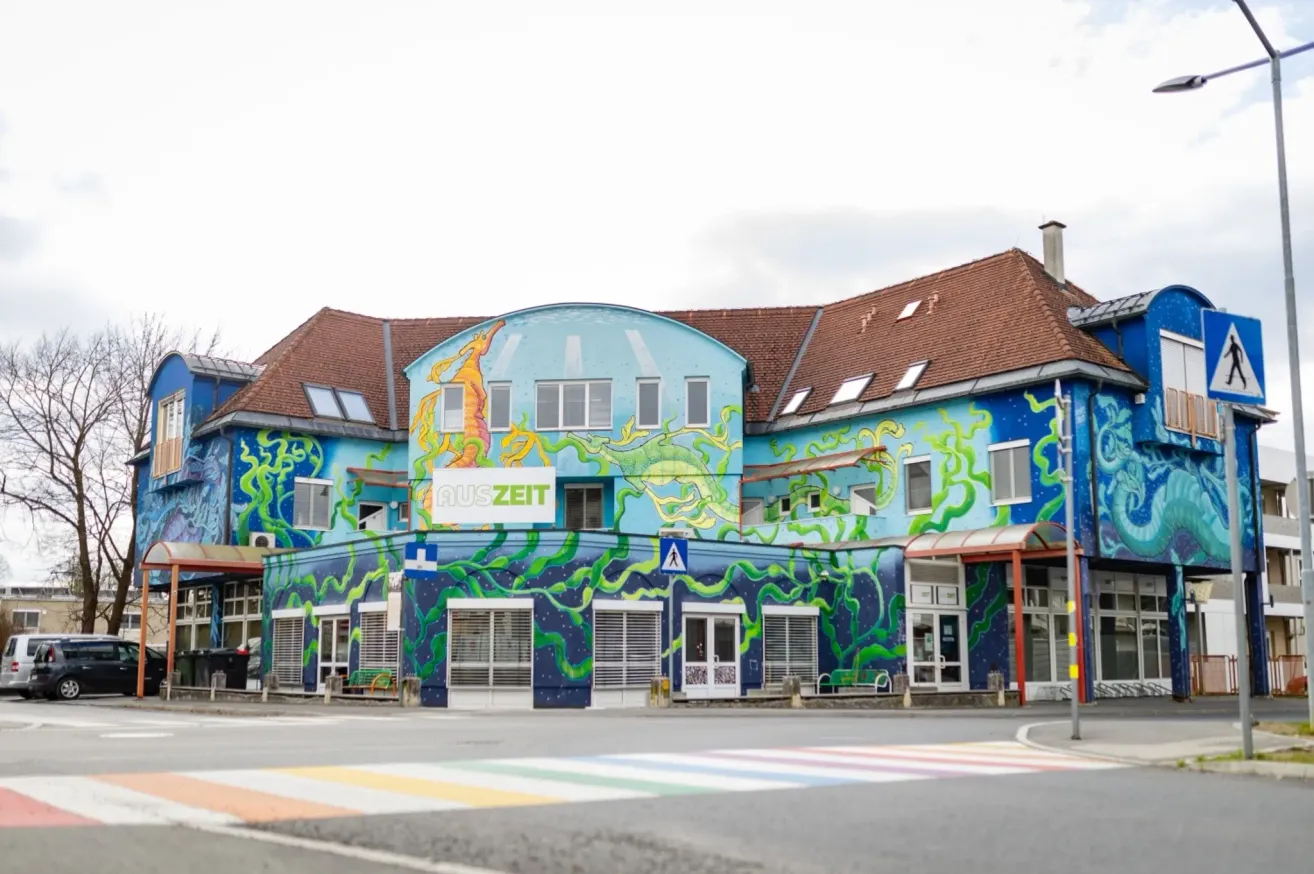 Ein blaues Gebäude mit mehreren Fenstern und einem Schild mit der Aufschrift 'AUSZEIT'. Es zeigt ein großes Wandbild mit Seetieren.