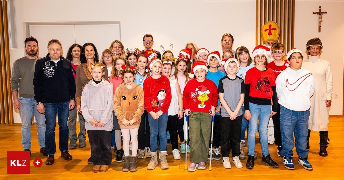 Eine Gruppe von Menschen, einschließlich Kindern und Erwachsenen, posiert für ein Foto in Weihnachtsmützen und Winterkleidung. Sie stehen in einem Raum mit Holzböden.