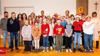 Eine Gruppe von Menschen, einschließlich Kindern und Erwachsenen, posiert für ein Foto in Weihnachtsmützen und Winterkleidung. Sie stehen in einem Raum mit Holzböden.