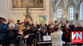 Ein Chor aus Erwachsenen in Winterkleidung singt in einer Kirche, mit einem Pianisten und einem Gemälde dahinter.