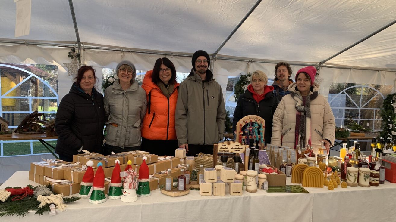 Mehrere Menschen stehen unter einem Zelt und lächeln. Vor ihnen steht ein Tisch voller verschiedener Produkte.