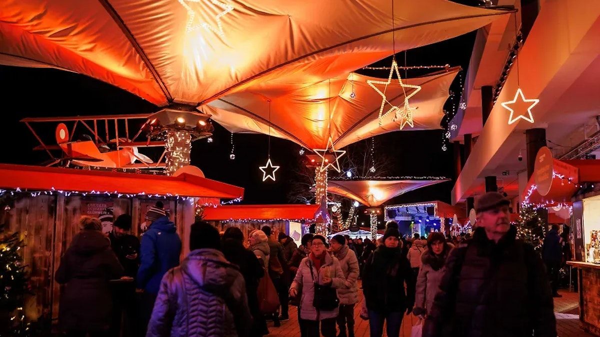 Ein geschäftiger Nachtmarkt mit beleuchteten Zelten, Sternendekorationen und Menschen, die unter orangefarbenen Lichtern einkaufen.