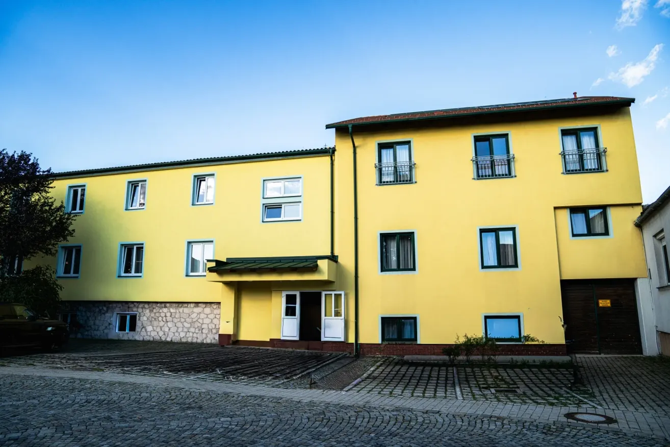 A yellow building with multiple windows and a brick pathway in front, under a clear blue sky.