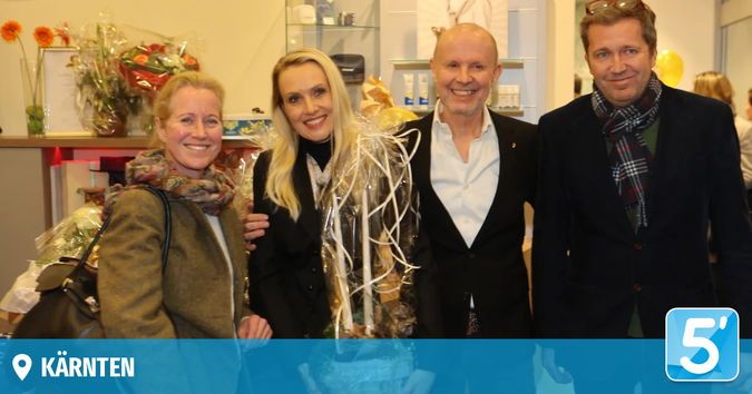 Vier Menschen lächeln und posieren für ein Foto in einem Raum. Zwei Frauen und zwei Männer. Ein Blumenstrauß und ein Schild sind im Hintergrund.