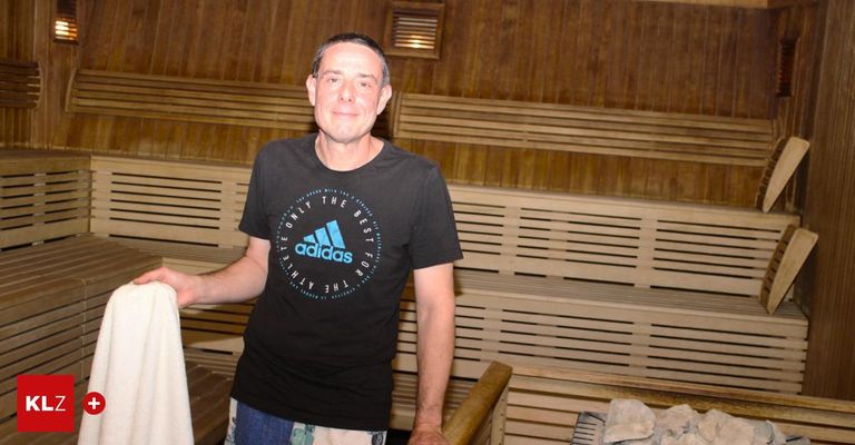 Ein Mann in einem Adidas-T-Shirt steht vor Holzbänken in einer Sauna.