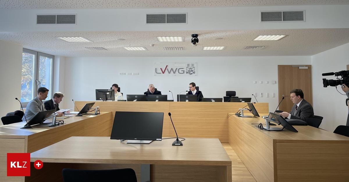 Ein Konferenzraum mit vier Personen, die an einem Tisch sitzen, jeder mit einem Mikrofon und einem Monitor. Der Raum hat eine große weiße Wand mit dem LVWG-Logo und mehrere Deckenleuchten.