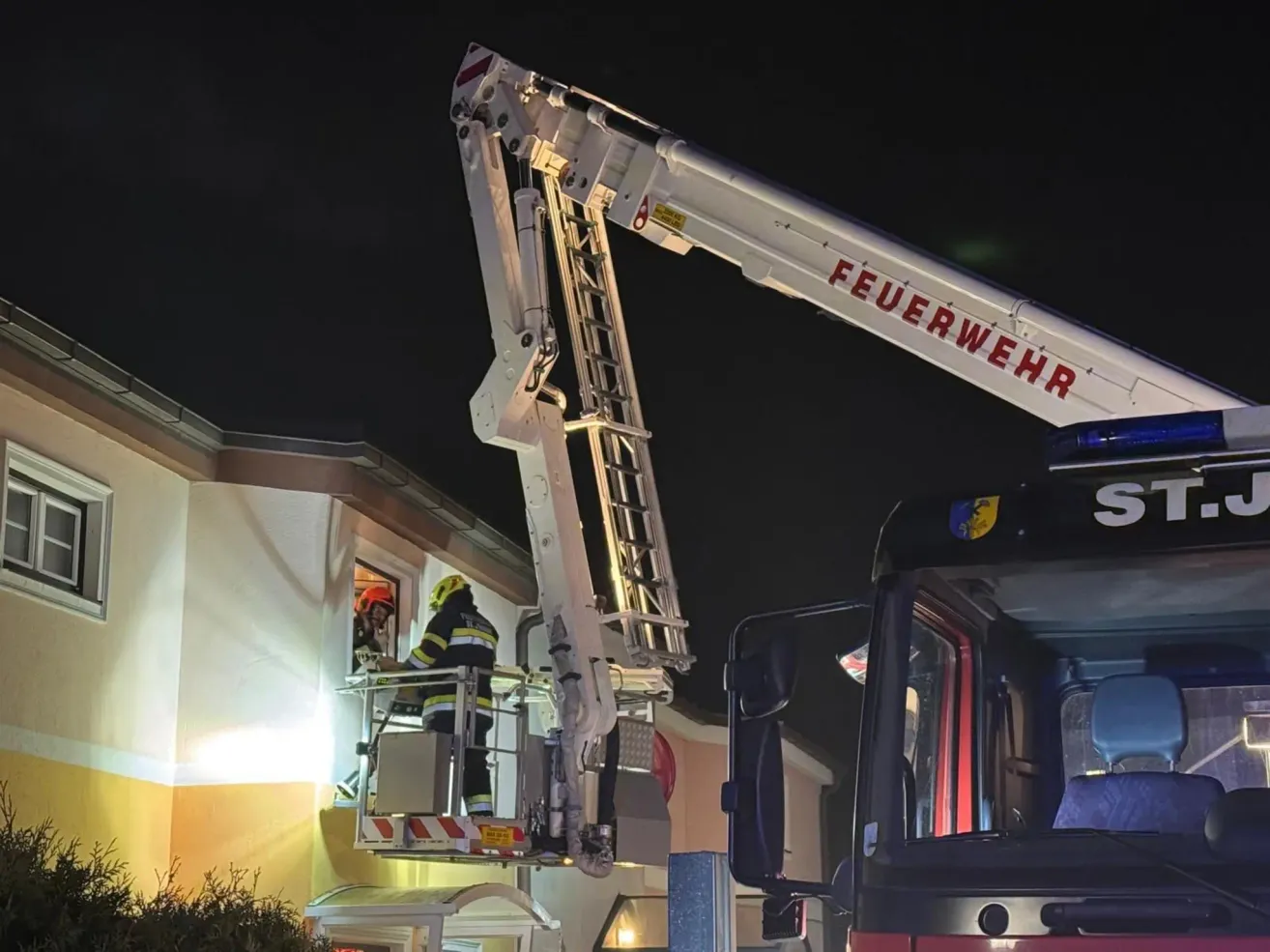 Ein Feuerwehrmann steht auf einer Leiter, die aus einem Feuerwehrwagen ragt und rettet möglicherweise jemanden aus einem Fenster bei Nacht.
