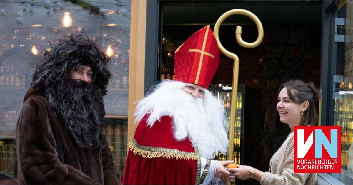 Eine Person, die als Weihnachtsmann verkleidet ist, steht vor einem Gebäude mit einer Frau und einer weiteren Person.