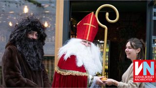 Eine Person, die als Weihnachtsmann verkleidet ist, steht vor einem Gebäude mit einer Frau und einer weiteren Person.