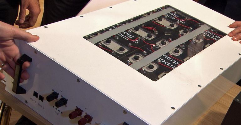 Ein weißes elektronisches Gerät mit mehreren schwarzen und roten Kabeln, die mit einer Reihe von Batteriezellen mit den Bezeichnungen 'Power' und 'Amper' verbunden sind, ist zu sehen.