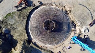 Eine Draufsicht auf eine kreisförmige Baustelle mit Metallgerüsten. In der Mitte befindet sich eine große kreisförmige Öffnung. Die Baustelle ist von Erde umgeben und hat einige Geräte und Strukturen im Hintergrund.