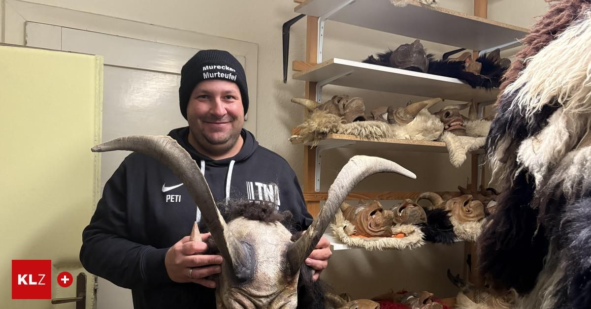 Ein Mann in einem schwarzen Hoodie mit Hörnern steht in einem Raum mit Regalen voller Tiermasken und Hörnern. Er lächelt und hält eine maskierte Hornmaske.