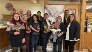 Eine Gruppe von Erwachsenen in formeller Kleidung stehen gemeinsam, Blumen haltend, lächelnd und posierend für ein Foto in einem Raum mit Holzbalken und einem Banner dahinter.