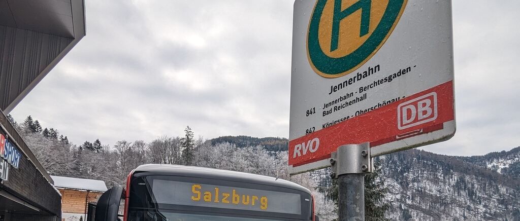 Ein Bus mit Salzburg auf der Frontscheibe steht vor einem Schild in einer verschneiten Bergregion.