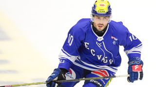 Ein Eishockeyspieler in einem blauen Trikot mit der Nummer 10 auf dem Rücken fährt auf dem Eis. Er hält einen Schläger in der rechten Hand.