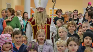 Eine Gruppe von Kindern und Erwachsenen versammelt sich um einen als Bischof verkleideten Mann. Der Mann hält einen Stab mit einem goldenen Kreuz.