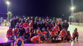 Eine Gruppe von Eishockeyspielern in roten und blauen Trikots und Helmen posiert für ein Foto auf einer Eisbahn bei Nacht.