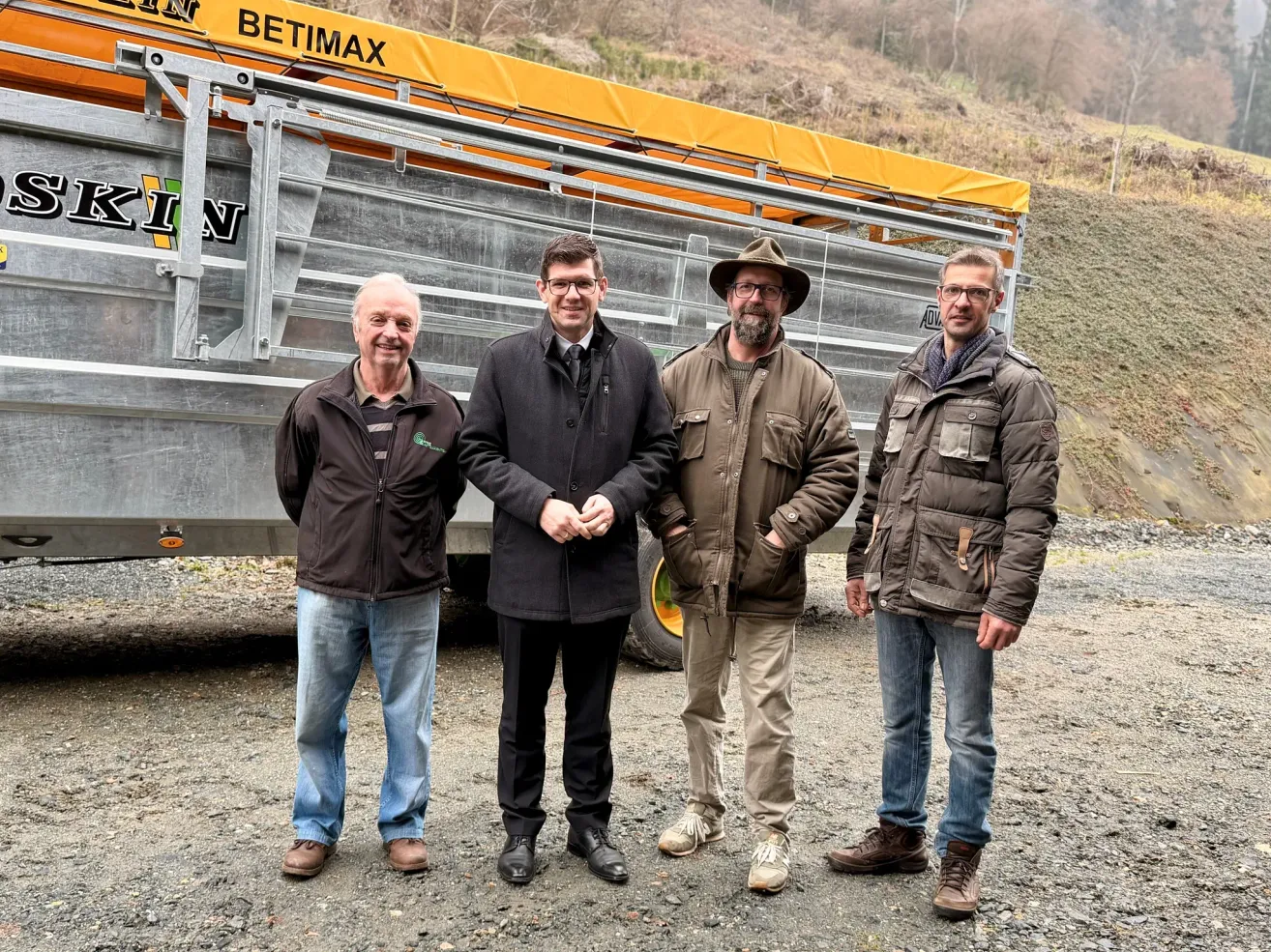 Vier Männer stehen vor einem großen, gelben BETIMAX-Truck, lächelnd und posieren für ein Foto. Sie sind in Winterkleidung gekleidet, mit verschiedenen Jacken- und Schuhstilen.