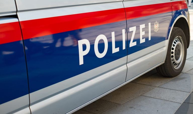 Ein Nahaufnahme eines Polizeifahrzeugs mit einem blau-weißen Streifen und dem Wort 'POLIZEI' in weiß auf einem roten Streifen. Die Fahrzeugtür zeigt das Wort 'POLIZEI' mit einer reflektierenden Oberfläche.
