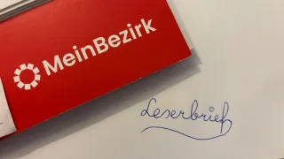 Ein roter Ordner mit der Aufschrift 'MeinBe zirk' liegt auf einem weißen Papier mit blauer kursiver Schrift, die 'Leverbrief' lautet.