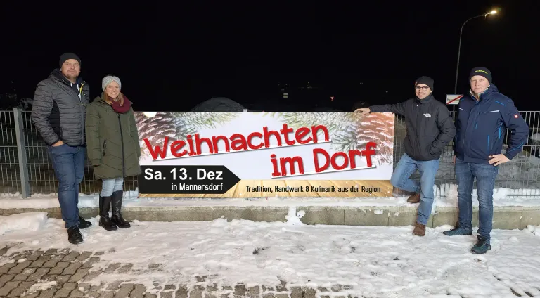Ein Banner für das Weihnachtsdorf-Event, geplant für Samstag, 13. Dezember, wird an einem verschneiten Tag im Freien ausgestellt. Eine Person steht daneben.