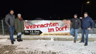 Ein Banner für das Weihnachtsdorf-Event, geplant für Samstag, 13. Dezember, wird an einem verschneiten Tag im Freien ausgestellt. Eine Person steht daneben.