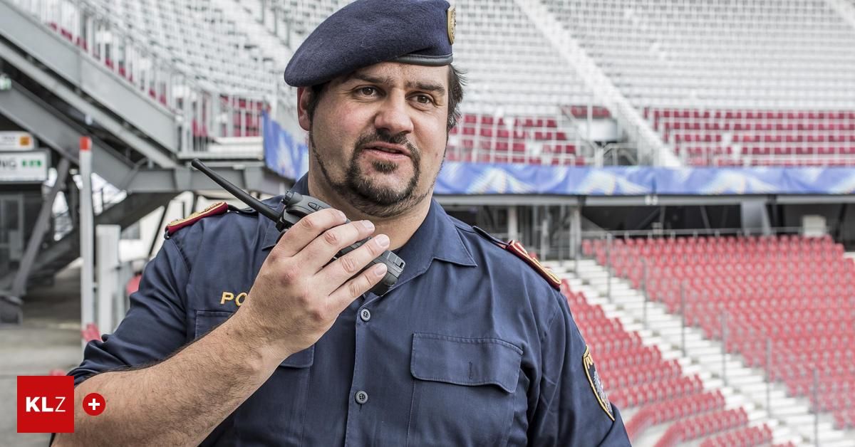 Ein Polizist benutzt ein Walkie-Talkie in einem Stadion mit leeren roten Sitzen im Hintergrund.