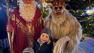 Eine Gruppe von Kindern und einem Erwachsenen posiert für ein Foto mit einem Mann als Weihnachtsmann und einer Person in einer Krampus-Verkleidung.