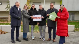 Sechs Personen posieren für ein Foto und halten Schilder mit den Texten Danke! und Neue Eisenstadter Stadter. Sie sind in Winterkleidung gekleidet und scheinen vor einem Gebäude zu stehen.