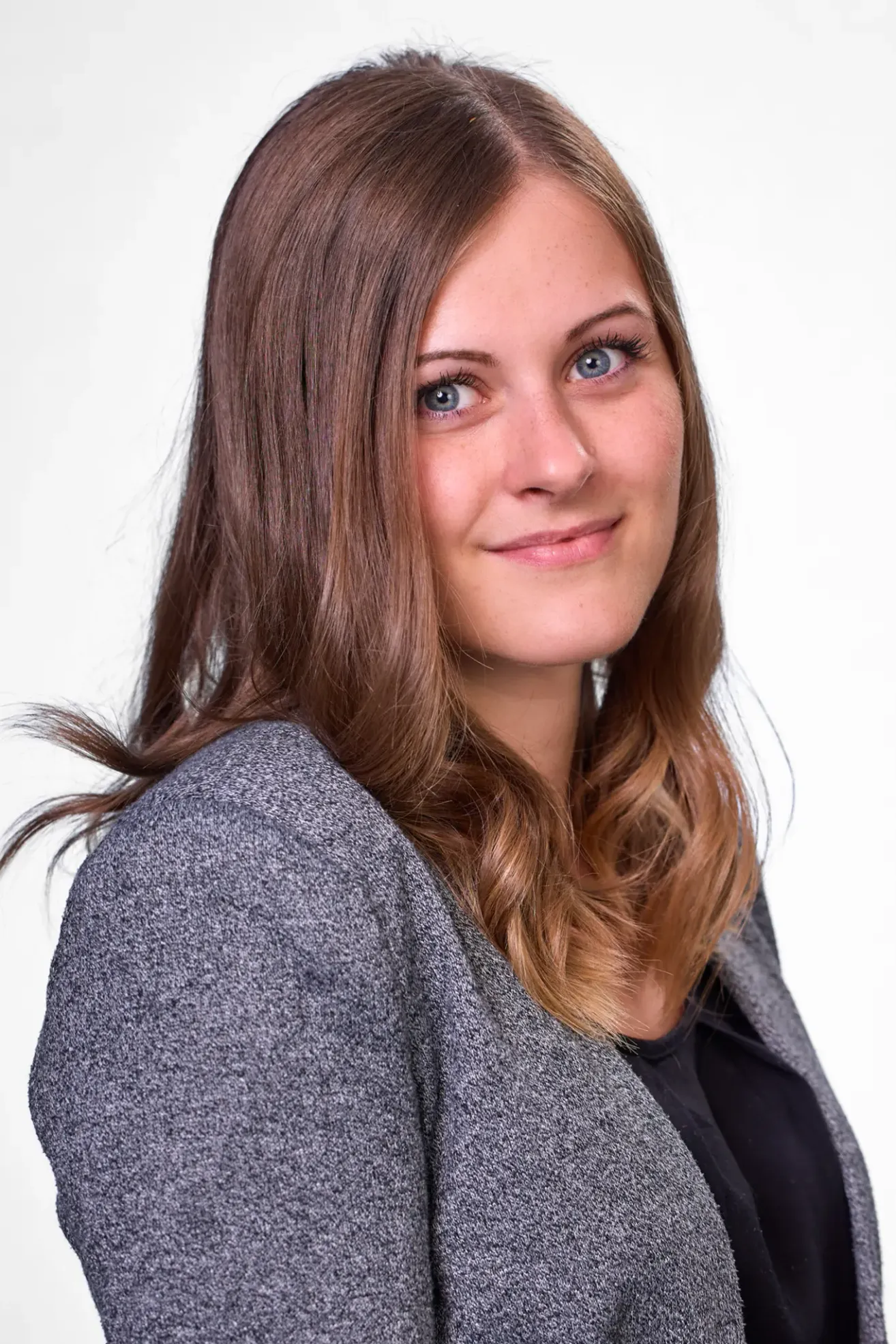 Eine Frau mit braunen Haaren und blauen Augen lächelt in die Kamera. Sie trägt einen grauen Cardigan.