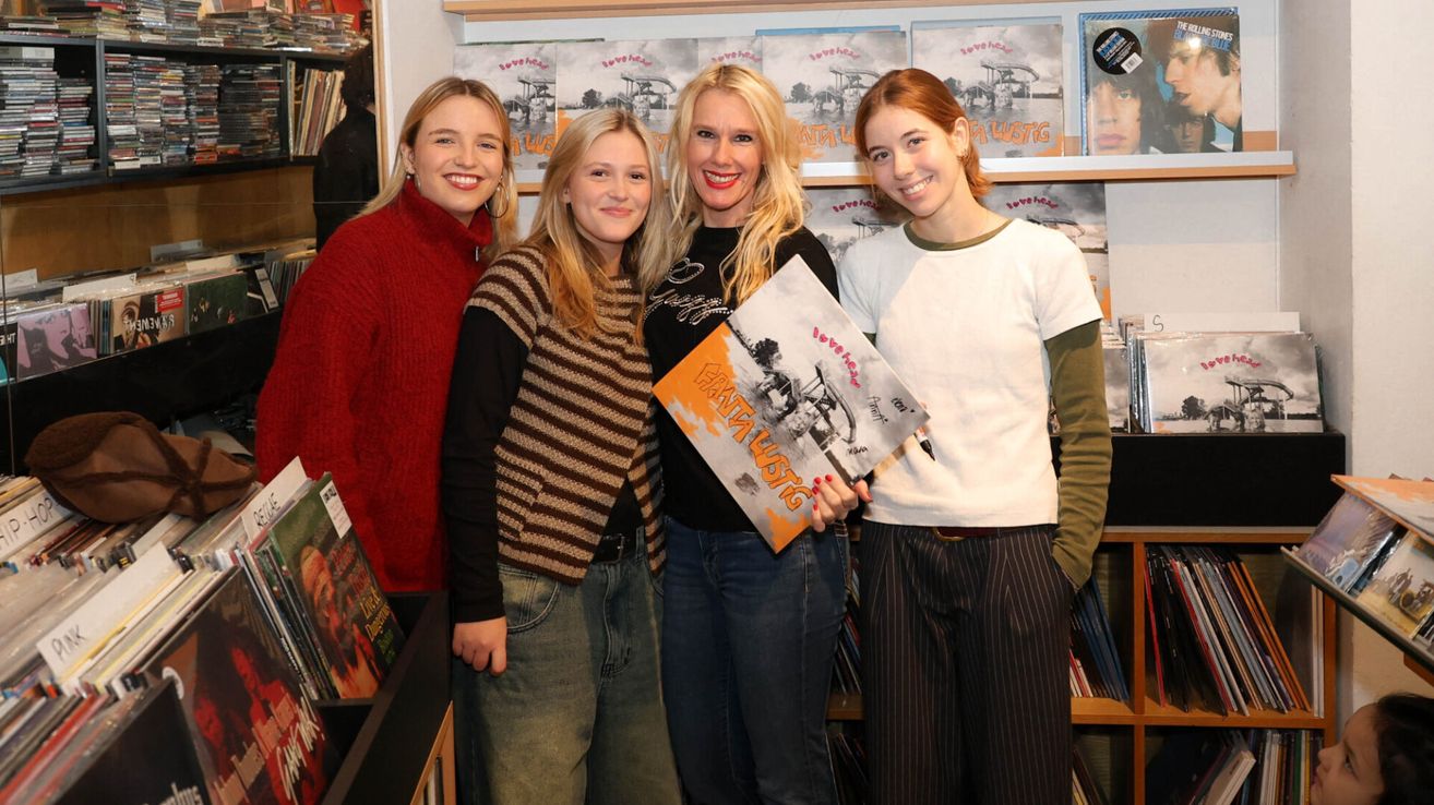 Vier junge Frauen stehen lächelnd zusammen in einem Geschäft. Eine hält ein Buch mit dem Titel 'Taste Music'. Hinter ihnen sind Regale mit Büchern und Zeitschriften gefüllt.