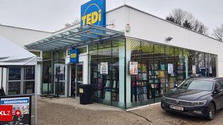 Ein TEDI-Laden mit einer Glasüberdachung und Regalen voller Bücher. Ein schwarzer Wagen ist davor geparkt.