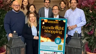 Gruppe von Menschen steht auf Stufen und hält ein Schild für Candlelight Shopping. Sie lächeln und posieren für ein Foto.