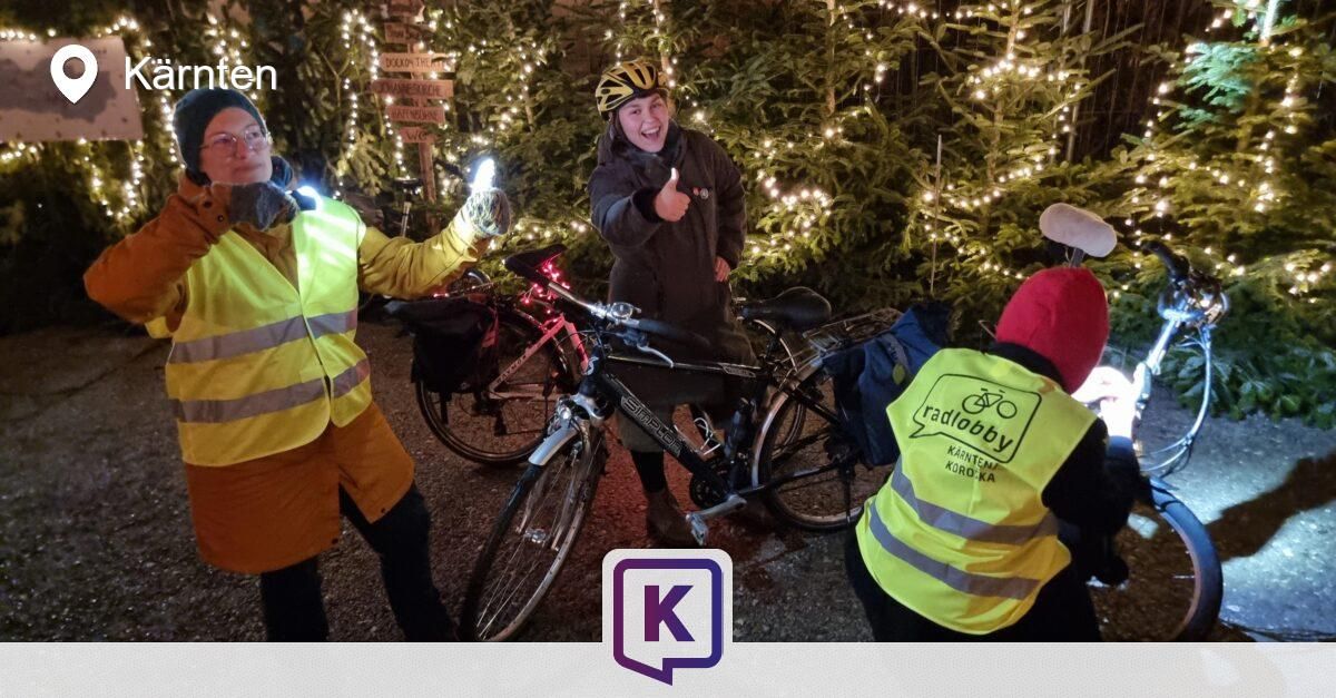 Drei Personen stehen um Fahrräder in einem Wald. Sie tragen Warnwesten. Eine Person gibt einen Daumen hoch. Hinter ihnen sind beleuchtete Bäume.