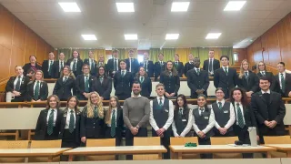Eine Gruppe von Schülern und zwei Lehrern in formeller Kleidung posiert für ein Foto im Klassenzimmer.