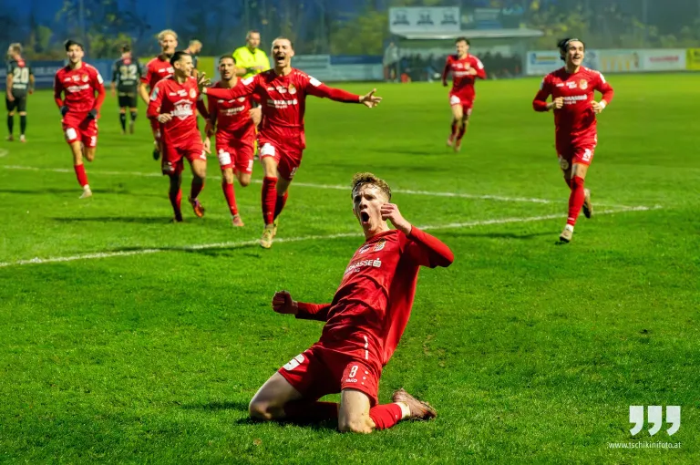Eine Fußballmannschaft feiert ein Tor auf einem Feld bei Nacht. Der Spieler im Vordergrund, Nummer 8, kniet vor Freude.