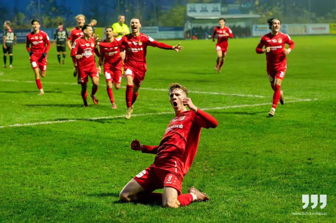 Eine Fußballmannschaft feiert ein Tor auf einem Feld bei Nacht. Der Spieler im Vordergrund, Nummer 8, kniet vor Freude.