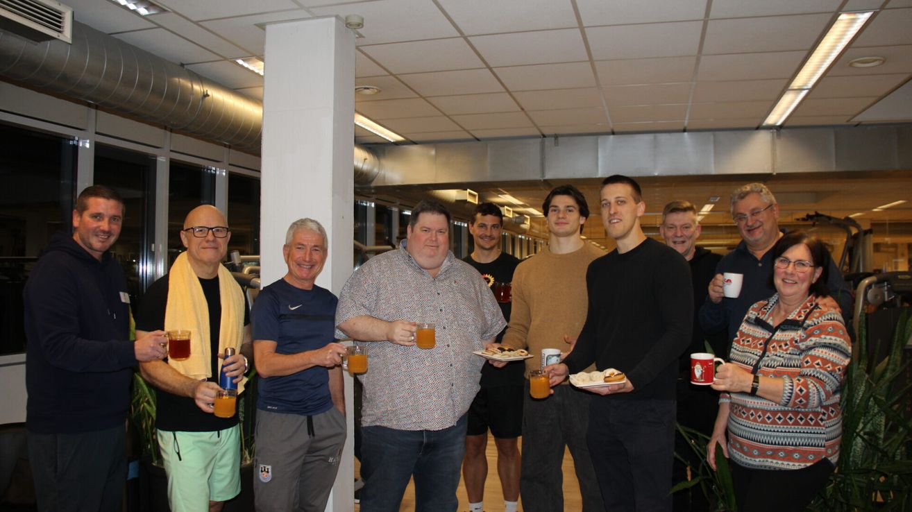 Eine Gruppe von Menschen steht zusammen, hält Tassen und Teller mit Essen und befindet sich in einer Innenumgebung.