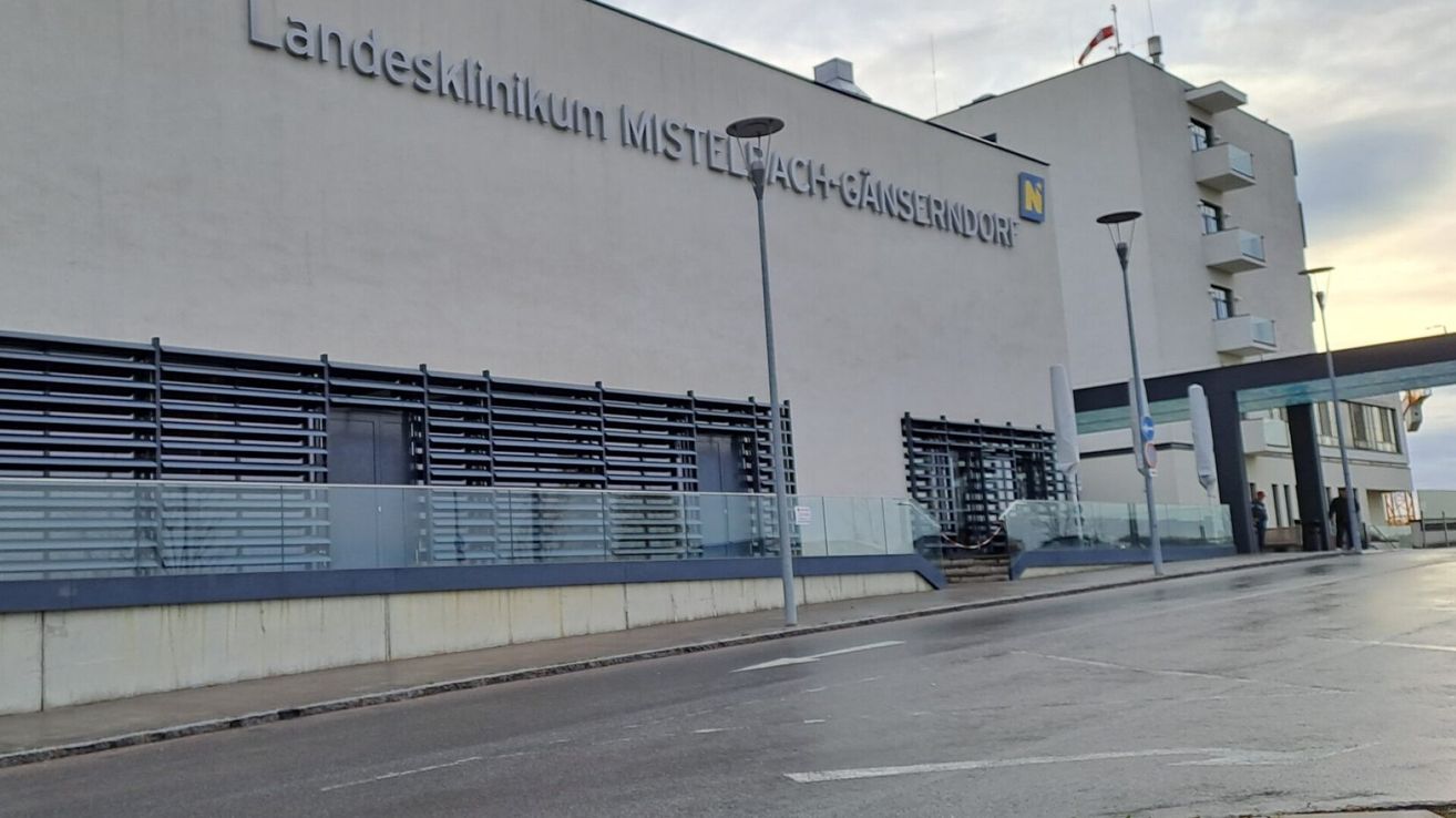 Ein Gebäude mit einem Schild, das 'Bundesklinikum Mistelbach-Gänserndorf' steht. Das Gebäude hat Glastüren und Fenster, eine Fahne oben und Straßenlampen davor.