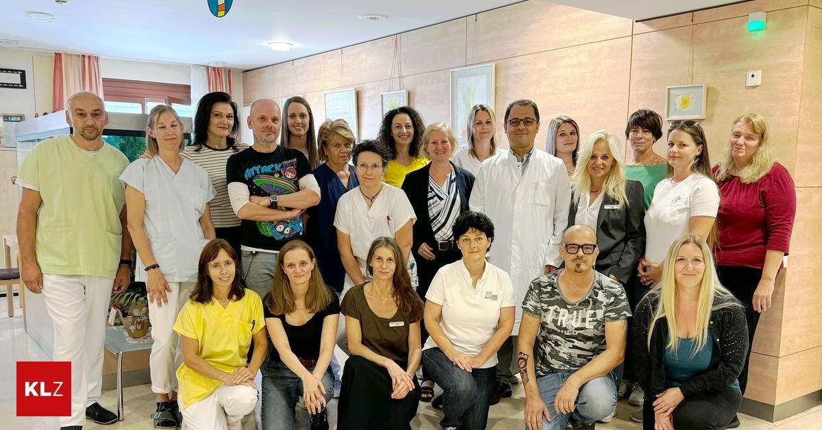 Eine Gruppe von medizinischem Fachpersonal und Mitarbeitern, darunter einige in weißen Kitteln, posiert für ein Foto in einem Raum mit beigen Wänden.